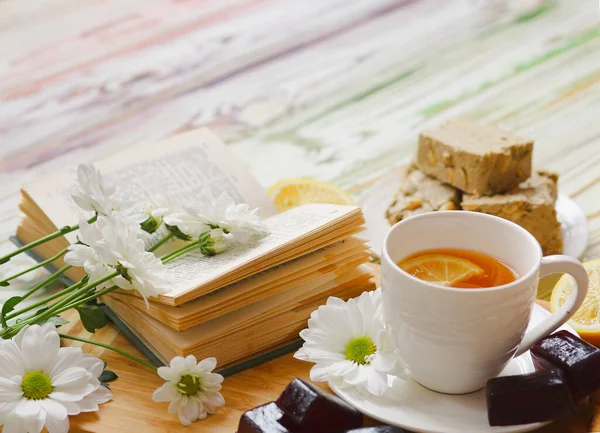 Banner with a breakfast: tea, sweets, lemon, marmalade on a beautiful light wooden background and decorate are book and flowers. Sweets. Sunlight from the window. Morning concept