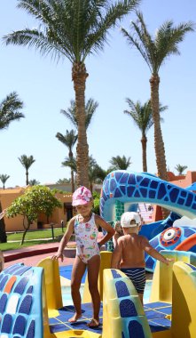 Küçük çocuklar havuzun olduğu yerde su kaydırağında oynarlar. Yaz eğlencesi. Tatil ve yaz konsepti.