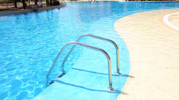 Background of blue transparent water in the swimming pool on the territory of the hotel. Descent to the pool with handrails. Rest and relaxation concept. Active rest by the sea.