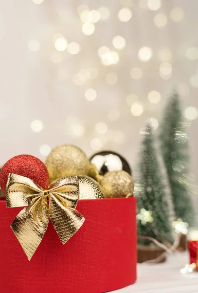 Bokeh, Noel ağaçları ve oyuncaklarının arka planında altın bir fiyonk olan kırmızı Noel hediyesi kutusu..