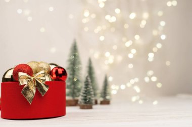 Bokeh, Noel ağaçları ve oyuncaklarının arka planında altın bir fiyonk olan kırmızı Noel hediyesi kutusu..