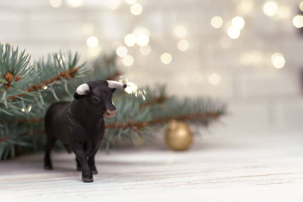 Decorative bull, symbol of the New Year on the background of Christmas trees and blue bokeh.