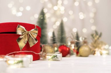 Bokeh, Noel ağaçları ve oyuncaklarının arka planında altın bir fiyonk olan kırmızı Noel hediyesi kutusu..