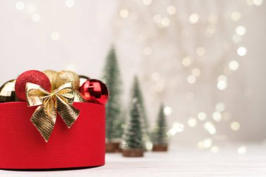 Bokeh, Noel ağaçları ve oyuncaklarının arka planında altın bir fiyonk olan kırmızı Noel hediyesi kutusu..