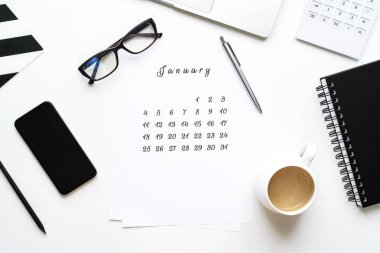 Ocak ayı takvimi beyaz masaüstünde bir fincan kahve ve bir defter beyaz çalışma alanıyla yatıyordu.