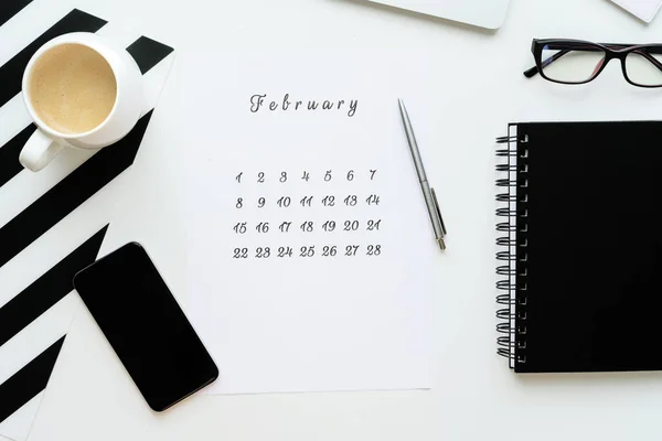 Calendario de febrero en el escritorio plano blanco yacía con una taza de café y un cuaderno, espacio de trabajo — Foto de Stock