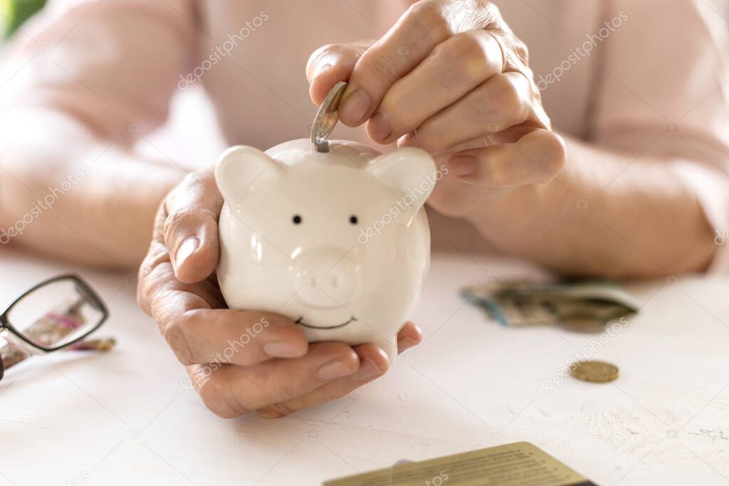 Old women's hands put money in the piggy Bank, the concept of retirement, savings.