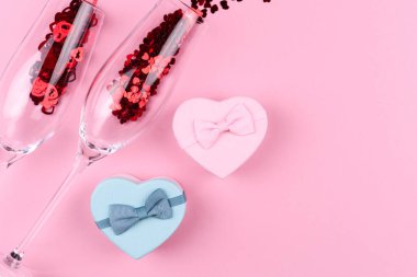 Kalp şeklinde pullarla dolu iki şampanya bardağı bir şişe şampanya ve pembe bir arka planda Sevgililer Günü hediyesi..