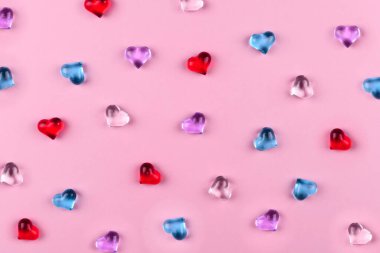 Sevgililer Günü için pembe zemin üzerinde renkli cam kalpler serpiştirilmiş.