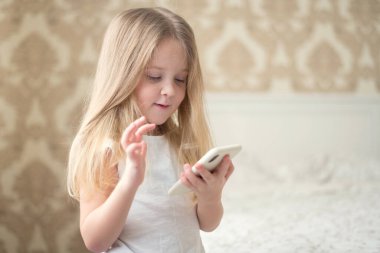 Küçük sarışın bir kız telefonda kalır ve sosyal internet oyunlarıyla oynar.