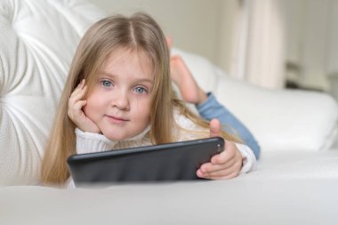 Yatakta sosyal internette tablet oynayan küçük bir kız. Küçük kızın dijital tabletten video izlemesini kapat.