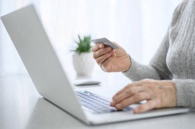Gündelik hayatta modern teknolojiyi kullanan üst düzey bir kadının elleri kredi kartıyla dizüstü bilgisayarda çalışıyor. çevrimiçi alışveriş