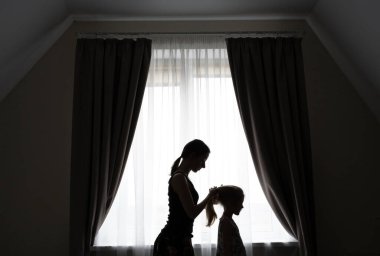 Kızının saçını tarayan şefkatli bir annenin silueti..