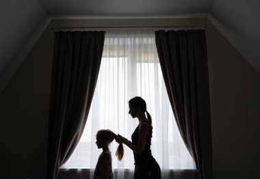 Kızının saçını tarayan şefkatli bir annenin silueti..