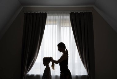 Kızının saçını tarayan şefkatli bir annenin silueti..