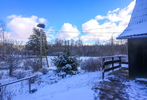 木製のポール 農村住宅の建物の詳細と雪に覆われたフィールド上のコウノトリの巣と冬の風景 — ストック写真