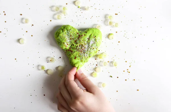 Green heart with shiny glitters made from slime by child