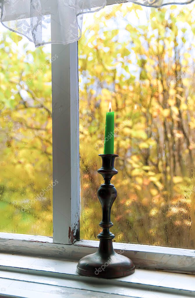 Burning wax candle in brass candlestick on the wooden window sill of in country house interior.
