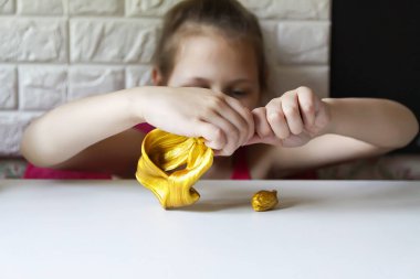Little girl playing with the gold slime. Sensory activity for child. clipart