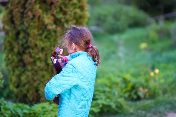 少女はギターを弾き 春には緑の草原で屋外で歌う 田舎の庭の幸せな子供 — ストック写真