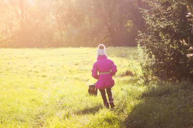 Küçük kız güneşli baharda açık havada aktif siyah köpekle yürüyor..