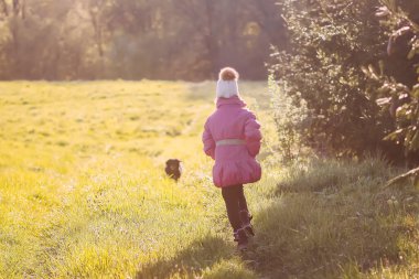 Küçük kız güneşli baharda açık havada aktif siyah köpekle yürüyor..
