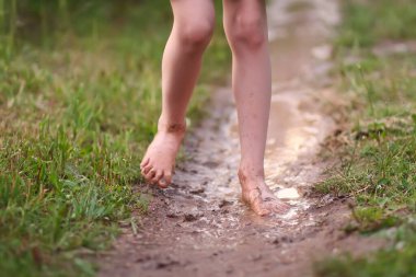 Kırsal kesimdeki yaz yağmurundan sonra çıplak ayaklı kız su birikintilerinde yürüyor..