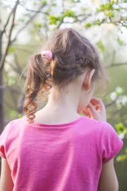 Bahar bahçesinde yürüyen bir kız çiçek açan kiraz ağaçlarıyla ılık altın günbatımı ışığında