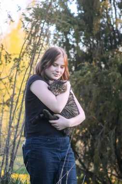 Kız, güzel çizgili gri kedisini bahar arka planında elinde tutuyor.