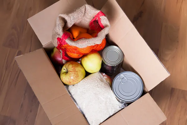 Tin cans, fresh apple fruits, buckwheat and rice packs in a cardboard box. Food donation, delivery theme.