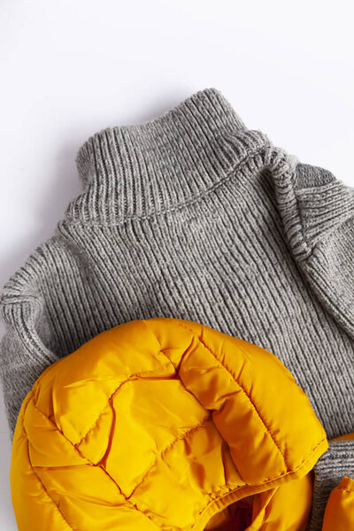 Warm yellow jacket and woolen knitted jumper on white background. Fashion outfit. Bright trendy colors. Home storage. Small space organizing
