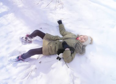 Little happy girl lying on fresh snow in winter forest