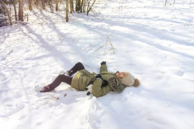 Little happy girl lying on fresh snow in winter forest