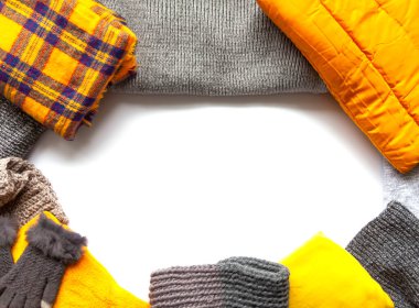 Beyaz arka planda sıcak kış giysileri. Uzayı kopyala Sarı ve gri moda renkleri. Örgü kazaklar, ceketler, eldivenler ve ekoseler.