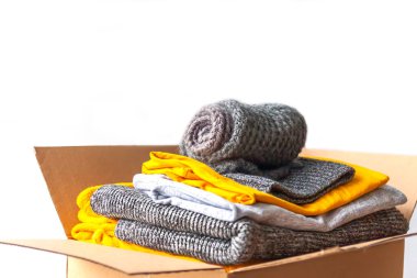 Karton kutudaki giysiler. Sarı ve gri moda renkleri. Yuvarlak tişörtler ve kazaklar. Ev kıyafetleri kompakt düzenleme. Ev deposu