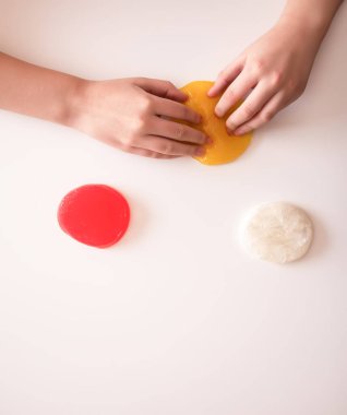 Işığın altında yumuşak, parlak balçık geren eller. Renk, doku ve hayal gücünü ifade eder.