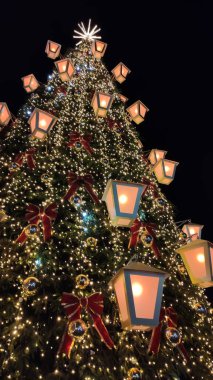 Kar, dekore edilmiş bir Noel ağacının tabanını hafifçe kaplıyor. Sahne cazibesini, sıcacık kış havasını ve mevsimsel neşesini yansıtıyor..