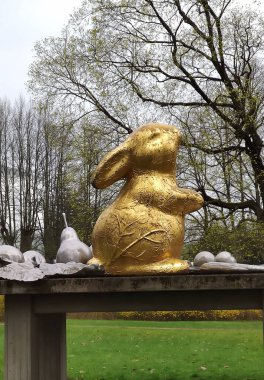 Riga, Letonya - 20 Nisan 2025: Botanik bahçesindeki ahşap bir masada gümüş meyveli bir Paskalya tavşanı heykeli.