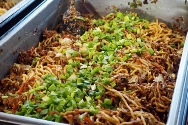 Et soslu Asya eriştesi ve dünya mutfağı festivalinde metal bir kapta yeşil soğan. Sokak yemeği.