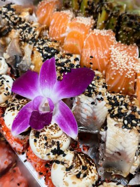 Canlı mor bir orkide çiçeğiyle süslenmiş taze somon, yılan balığı ve havyarla süslü lüks suşi tabağı..