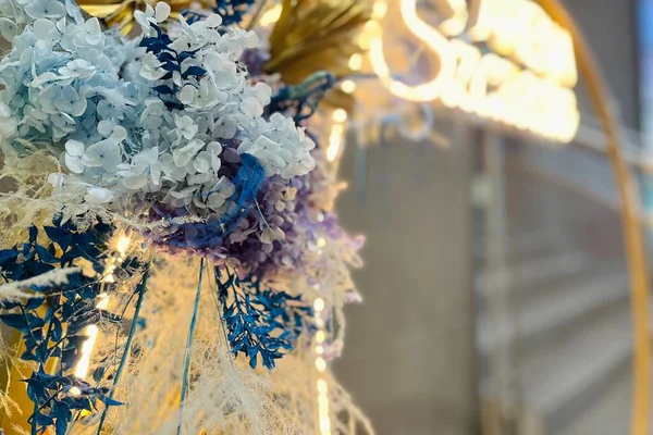 Parlayan ışıkları ve mavi, lavanta ve bej tonlarında korunmuş çiçeklerin çiçek düzeniyle yuvarlak metal çerçeveli lüks bir dekor..