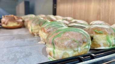 Yumuşak şeker jöleli kremalı çörekler ve yeşil çiseleme, fırın tepsisinde soğutma. Yakın çekim, yumuşak doku ve sıcak tonlar. Profesyonel fırın, el yapımı tatlı ve şekerlemeler..