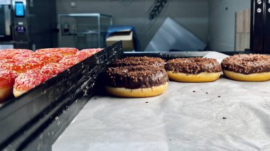 Üstü parlak çikolata kaplı kremayla kaplı donut seçimi. Parşömen kağıdında sergilenen çikolatalı çörek, gurme tatlı çeşitleri, modern pastane vitrinleri..