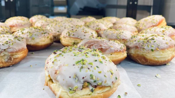 Süslü, beyaz kremalı ve şam fıstıklı bir sıra jöleli çörek. Minimalist kompozisyon, seçici odaklanma ve doğal ışık. Taze tatlı, modern fırın iş akışı ve tatlı yemek fotoğrafçılığı..
