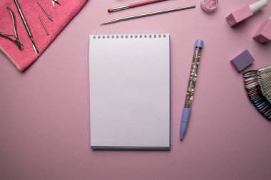 Pembe zemin üzerinde kalem ve manikür aksesuarları ile boş spiral defterin üst görünümü, düz yatıyordu