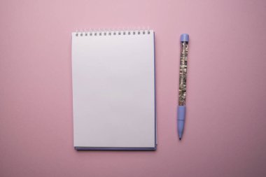 Pembe zemin üzerinde kalem olan boş spiral defterin üst görünümü, düz yatıyordu