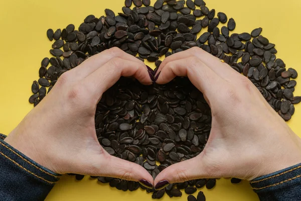 A pile of watermelon seeds on a yellow background in the shape of a heart.Watermelon seeds stacked in the shape of a heart, top view
