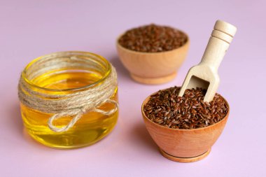 Tahta tabaklarda keten tohumu, pembe arka planda cam kavanozda keten yağı. Faydalı doğal yağ. Doğal ve sağlıklı gıda konsepti.