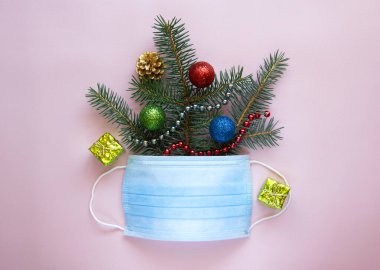 Noel ağacı dallarıyla yaratıcı kompozisyon, yılbaşı dekorasyonu ve yüz koruma maskesi. Virüslere, gribe ve koronavirüse karşı koruma. Tatil konsepti. Üst görünüm, alanı kopyala.