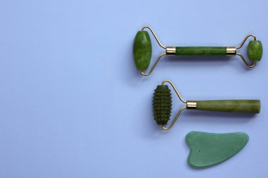 Mavi arka planda izole edilmiş iki kuvars yeşim taşı ve Gua sha taşı. Cilt bakımı yüz masajı ve rahatlama konsepti. Düz yat, boşluğu kopyala.